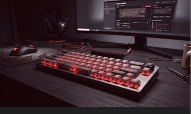 Una tastiera meccanica da gaming con retroilluminazione rossa su una scrivania in legno, accanto a un mouse e a un monitor che mostra un software di configurazione.